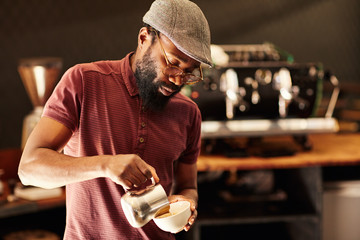 Skilled African barista pouring frothed milk into a cappucino