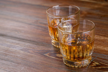 Glasses of whiskey with ice on wood.