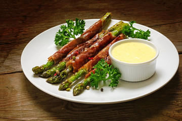 grilled green asparagus wrapped in prosciutto bacon on a rustic wooden table