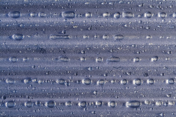 Water droplets on corrugated plastic with refracted light shinning through them at sunrise