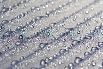 Water droplets on corrugated plastic with refracted light shinning through them at sunrise