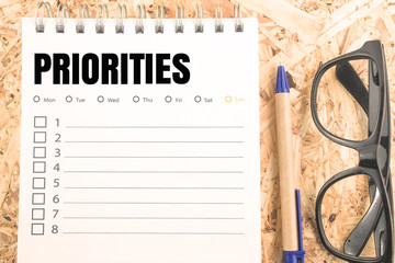 word prioritied check list on wooden table eyeglasses and pen background