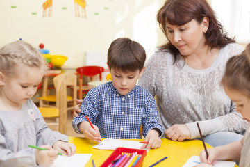 Cute pupil of the kindergarten, draws at the yellow table