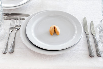 Fortune cookie on white plate with cutlery. Table served for a dinner. Selective focus