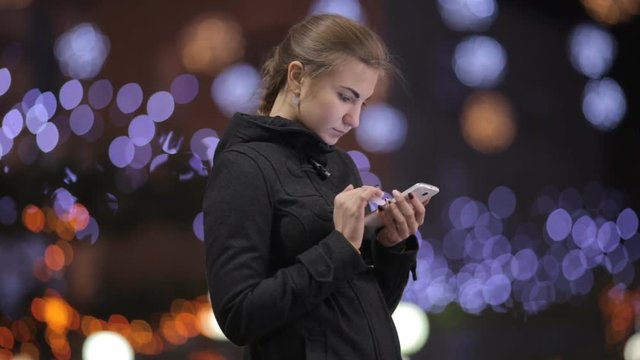 girl standing against a background of Christmas lights and use smartphones