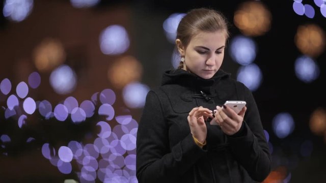 girl standing against a background of Christmas lights and use smartphones