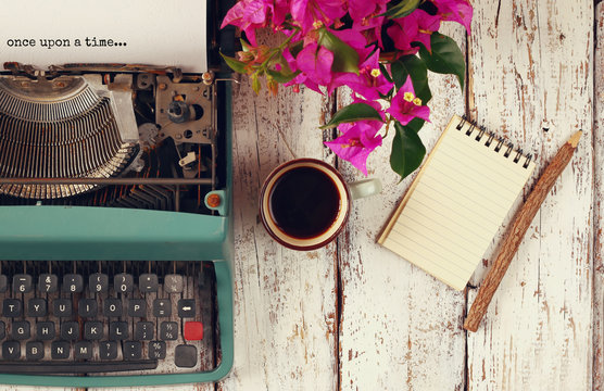 image of vintage typewriter with phrase "once upon a time", blank notebook, cup of coffee on wooden table