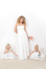 Fototapeta na wymiar Beautiful blond mom with two young daughters blondes in white dresses on a white background. Beautiful mother and daughters in studio