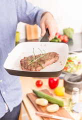 Pan with grilled steak and rosemary in man's or chef's hand