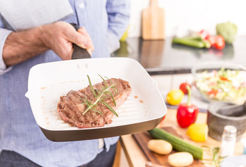 Pan with grilled steak and rosemary in man's or chef's hand