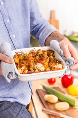 Roasting dish with hot chicken drumsticks in man's hands