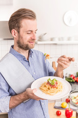 Happy smiling man eating spaghetti bolognese in the kitchen