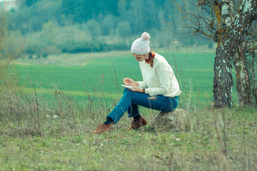 Usual pleasant hipster girl writes in a notebook. Dreamy girl on the nature