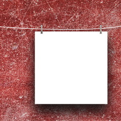 Close-up of one square blank frame hanged by pegs against red scratched wall background