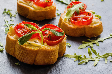 Toasts (Crostini) with ricotta, cherry tomatoes and arugula on black background. 