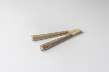 Two medical cannabis rolled joints on light background from side high angle