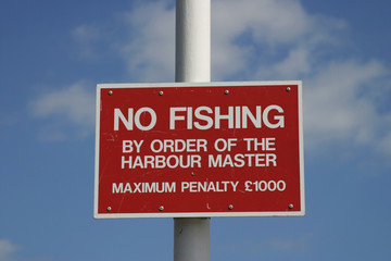 Obraz premium No fishing by order of the harbourmaster Maximum penalty £1000 sign against a blue sky.