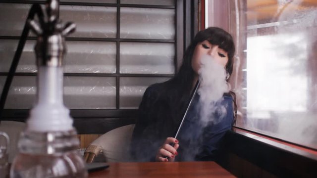 Beautiful young woman inhaling hookah. girl smoking shisha in cafe.