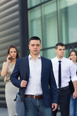 Portrait of confident young businessman in front of the group of busy business people on the move