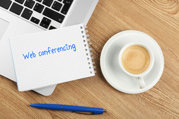 Web conferencing written in notebook, laptop and cup of coffee on table, top view