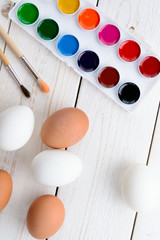 Chicken eggs and paints with brushes on the table