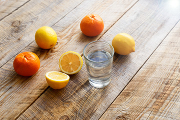 glass of water with lemons and oranges on wooden table