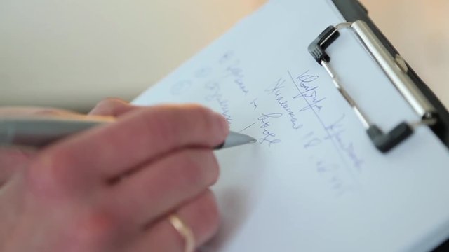 A man with a wedding ring records data on a sheet of paper.