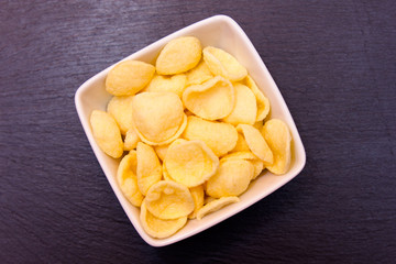 Potato snacks on a square bowl on slate top seen from above