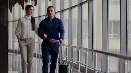 Happy loving couple in casual wear walking with a luggage by airport terminal. - Powered by Adobe