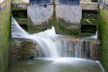 Canal lock cill with water spilling through gate. Lock with water escaping at high pressure through gaps, splashing onto cill