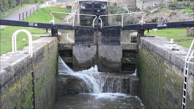 Canal lock cill with water spilling through gate. Lock with water escaping at high pressure through gaps, splashing onto cill