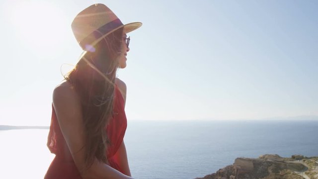 Tourist woman enjoying beautiful view of village Oia and sea before sunset. Young female is wearing sunglasses and sunhat. She is enjoying her summer vacation in Santorini.