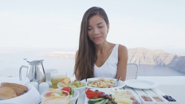 Breakfast table and luxury travel woman on santorini. Well balanced perfect breakfast table served at resort. Female tourist is looking at beautiful view of sea and caldera enjoying her vacation.