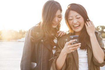 Two young women are laughing to see the smartphone together