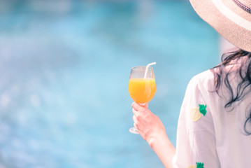 Rear view of beautiful woman in hat is holding orange juice glass in summer.