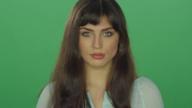 Beautiful brunette woman staring ahead, on a green screen studio background 