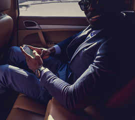 Black man in a sunglasses using smartphone in a car.