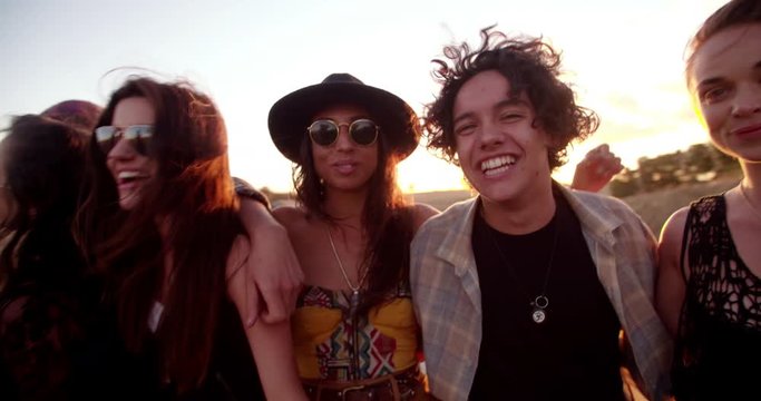 Teenage boho friends sitting on a convertible hood at sunset