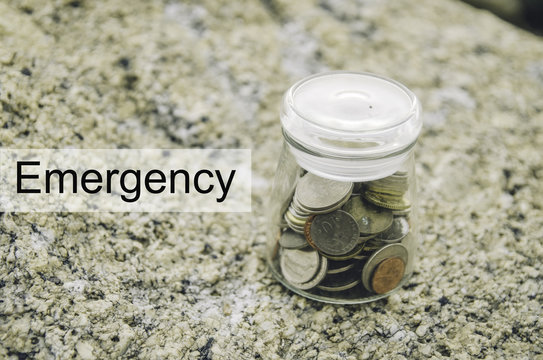 Financial image concept with word EMERGENCY. Blurred background coin in glass jar on the rock.