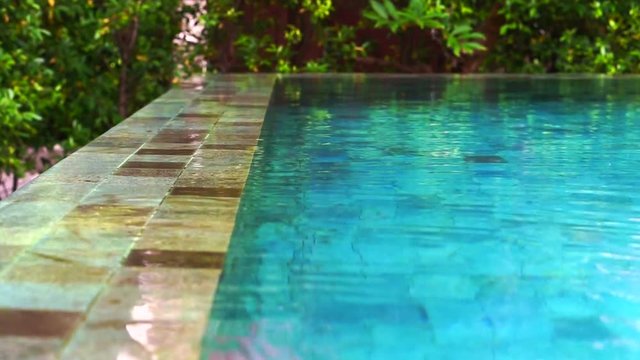 water flowing overflow on swimming pool edge system. Resort pond with natural stone decoration