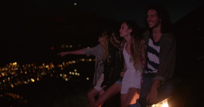 Teens hugging on a convertible looking at night city lights