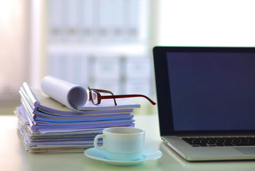 Laptop with stack of folders on table on white background