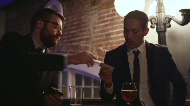A well dressed young man hands his business card to another man at a nightclub