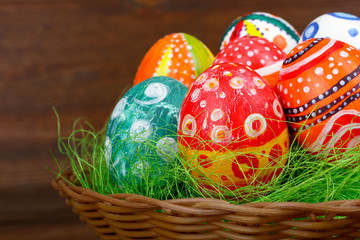 Easter eggs in beautiful and different colors lie on the grass in wicker basket on wooden background