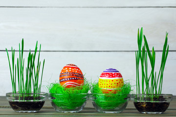 Easter eggs lying on the green grass in glass bowl on wooden background