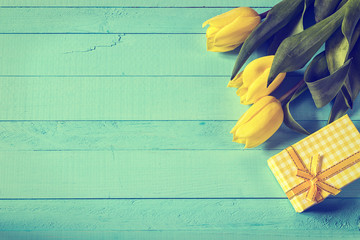 Yellow tulips and gift box with yellow ribbon on blue painted wo