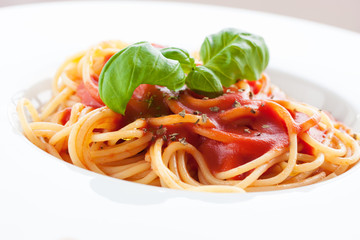 Tomato pasta spaghetti with fresh tomatoes, basil, italian herbs and olive oil in a white bowl on a white wooden background, closeup..