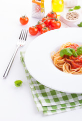 Tomato pasta spaghetti with fresh tomatoes, basil, italian herbs and olive oil in a white bowl on a white wooden background, closeup.
