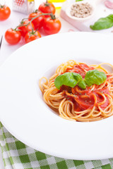 Tomato pasta spaghetti with fresh tomatoes, basil, italian herbs and olive oil in a white bowl on a white wooden background, closeup.