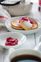 Summer cottage cheese pancakes on white plates on a wooden table with coffee, milk, sour cream and jam, closeup